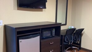 Ein kompakter Arbeitsraum mit einem an der Wand montierten Flachbildfernseher, einem kleinen Kühlschrank, einer Mikrowelle und einem Schreibtisch mit zwei Bürostühlen.
