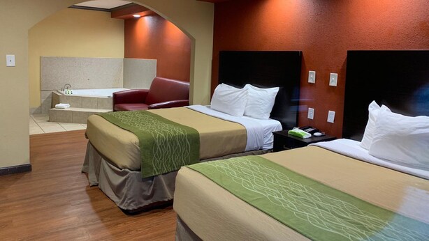 Ein Hotelzimmer mit zwei Betten, einer Sitzecke mit einem roten Sessel, einer Badewanne und einem kleinen Tisch mit Toilettenartikeln.