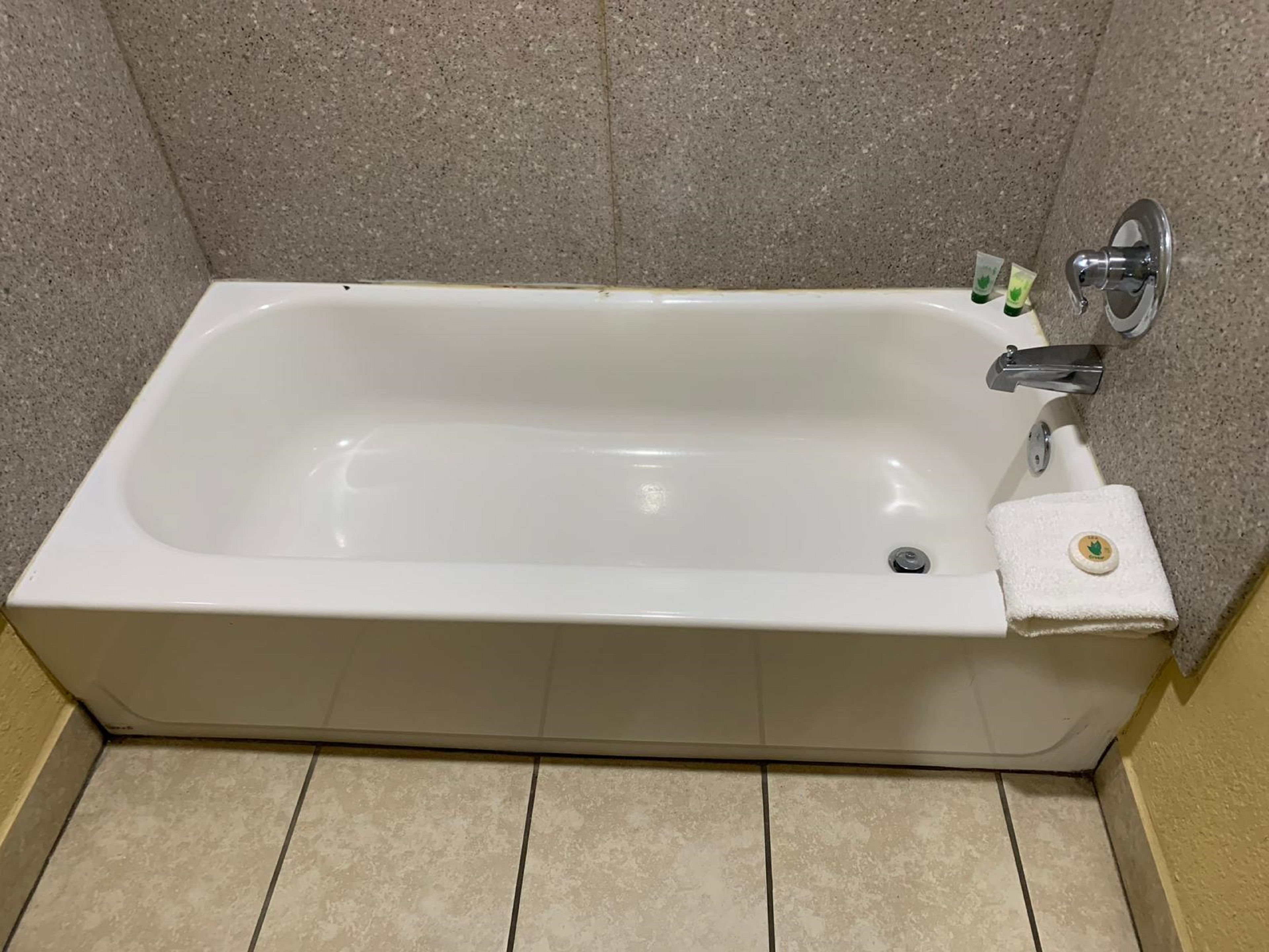 Uma banheira retangular com uma torneira cromada e uma pequena garrafa de shampoo ao lado.