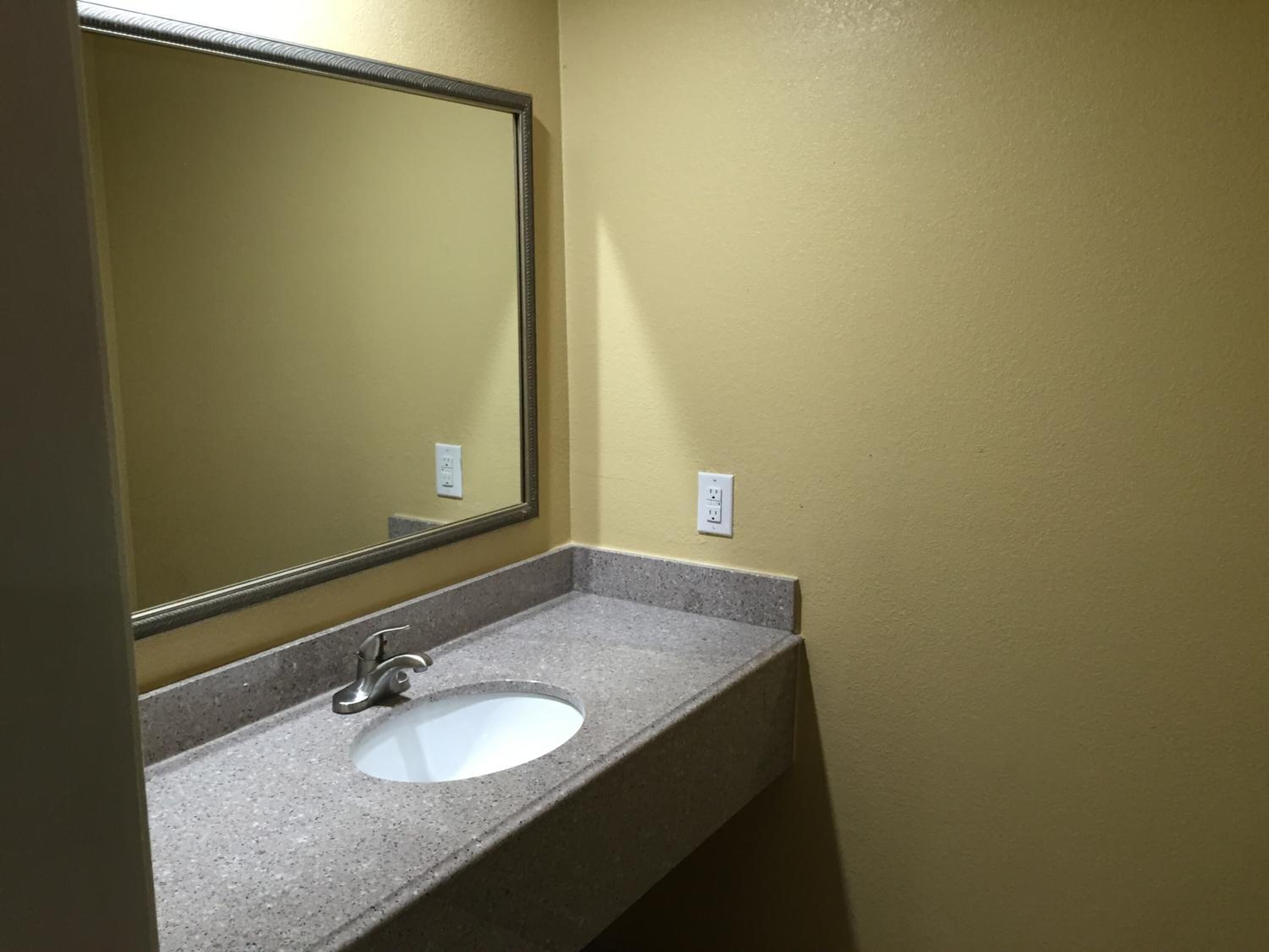 Une salle de bain avec un comptoir en granit, un lavabo blanc et un grand miroir.