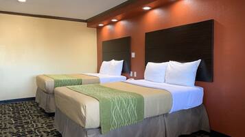 A hotel room with two beds, each with a green and beige bedspread, a dark headboard, and a patterned carpet.