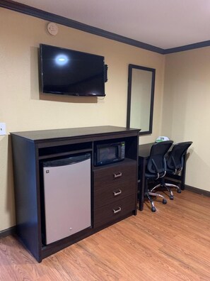 Habitación compacta con kitchenette, televisor de pantalla plana en la pared y un espejo.