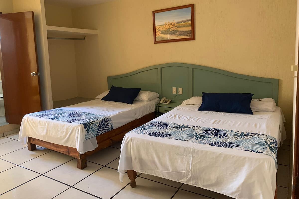 Ein Hotelzimmer mit zwei Betten, jeweils mit einem blumengemusterten Überwurf, einem grünen Kopfteil und einem Bild an der Wand.