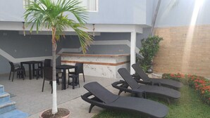 Een terras met lounge fauteuils, een bar en een kleine palmboom.