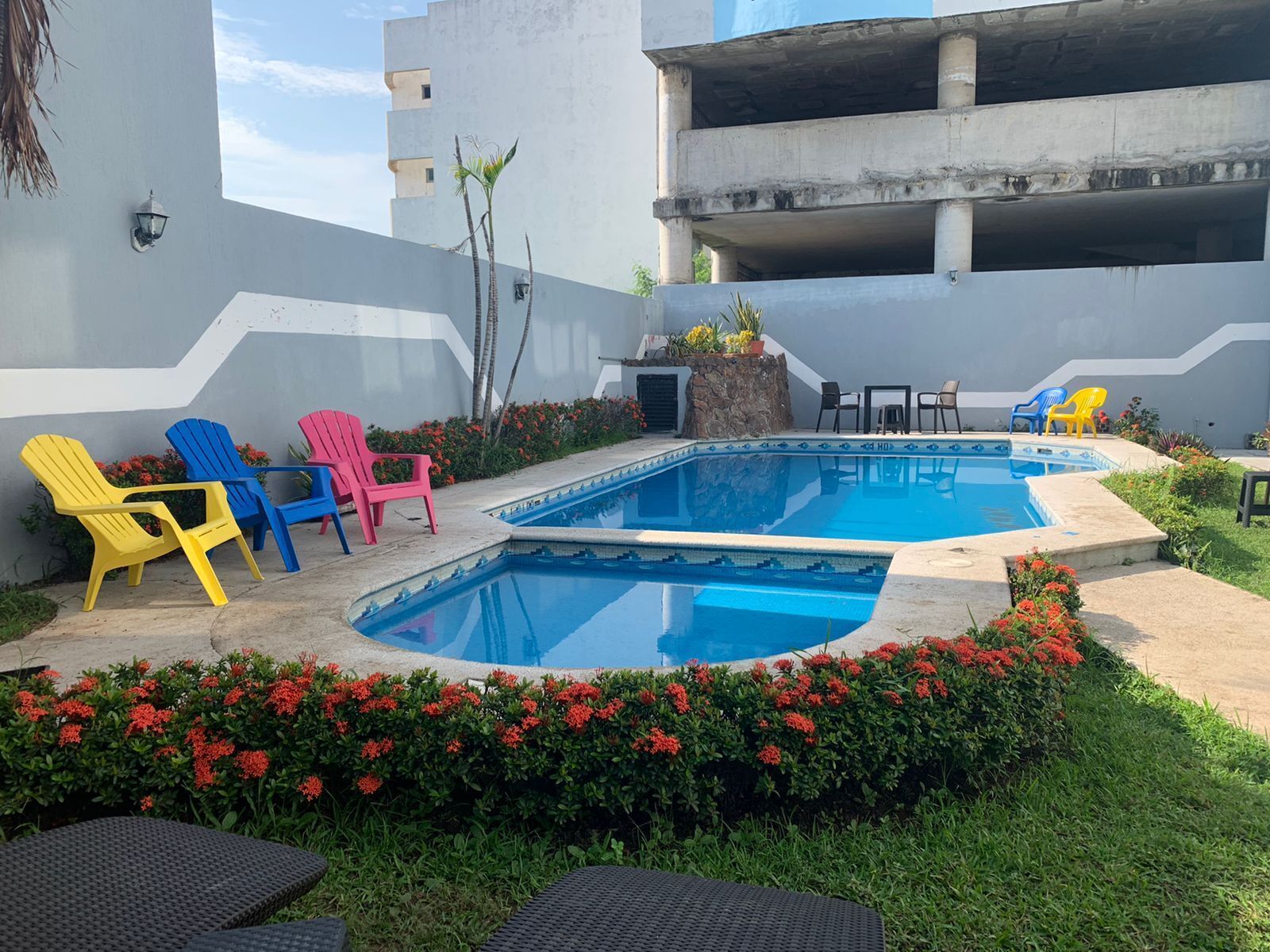 Piscina con sillones de descanso cercanos y una pequeña mesa, rodeada de follaje y flores.