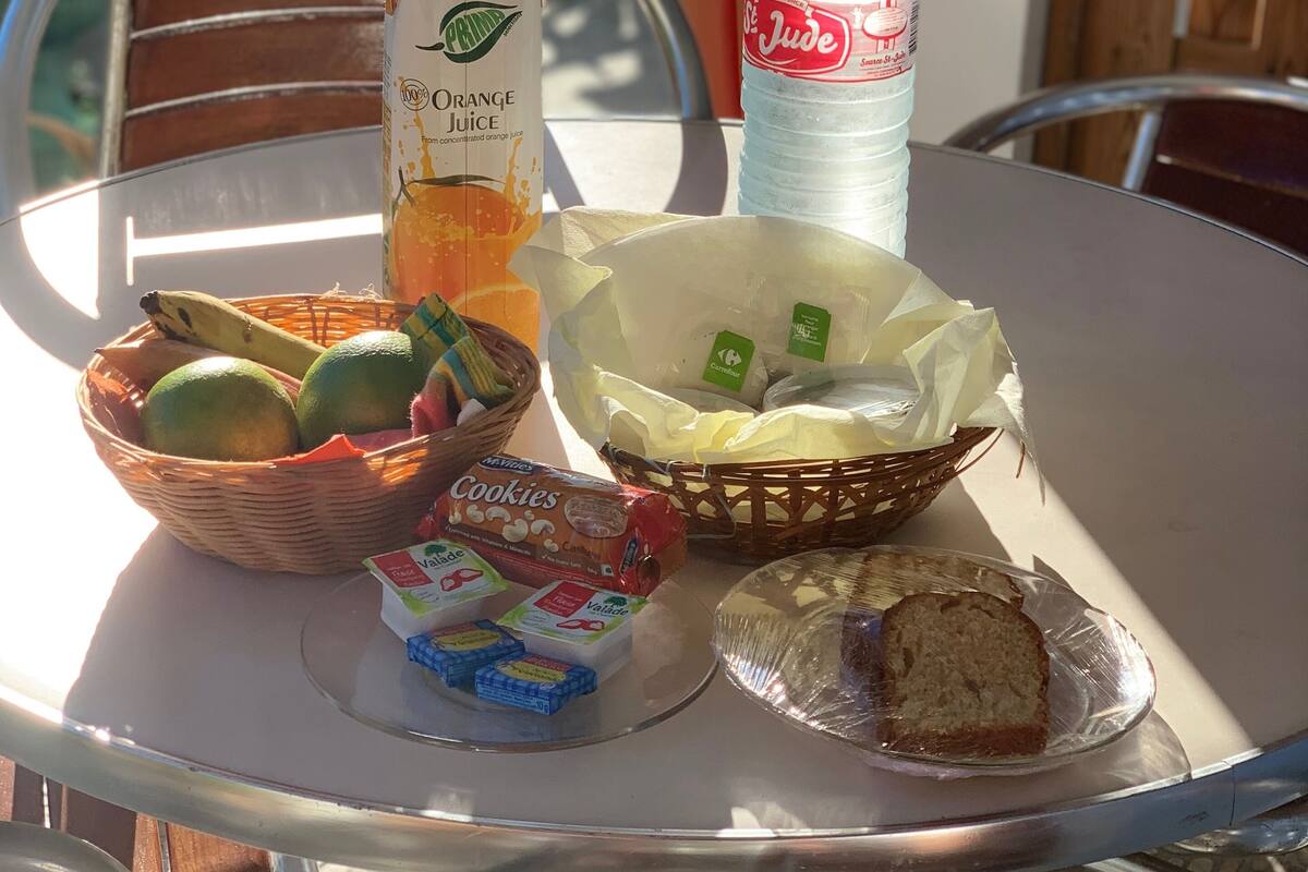 A table with a juice carton, a bottle of water, a basket of fruits, a packet of cookies, and a loaf of bread.