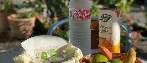 Uma mesa com uma garrafa de suco de laranja St. Jude's, um pacote de suco de laranja, uma cesta de frutas, um prato de pão e alguns lanches embalados.