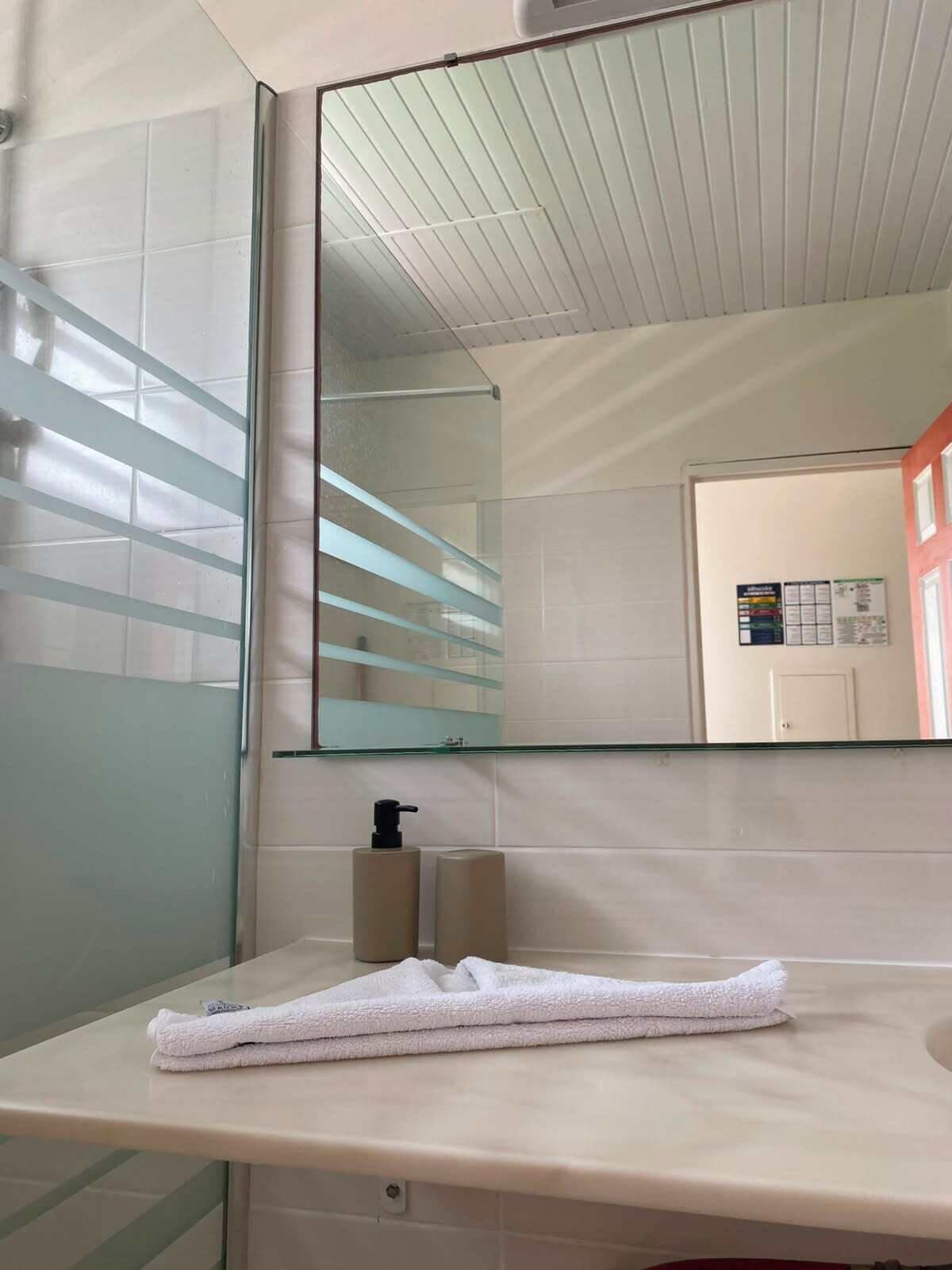 A bathroom with a large mirror, a towel on the counter, and a bottle of soap.
