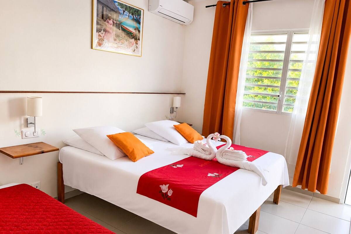 A hotel room with a bed, a nightstand, a wall-mounted lamp, a window with curtains, and a painting on the wall.