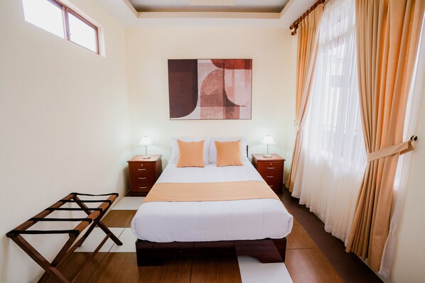 A neatly arranged bedroom with a large bed, two bedside tables with lamps, a wooden bench, and a window with curtains.