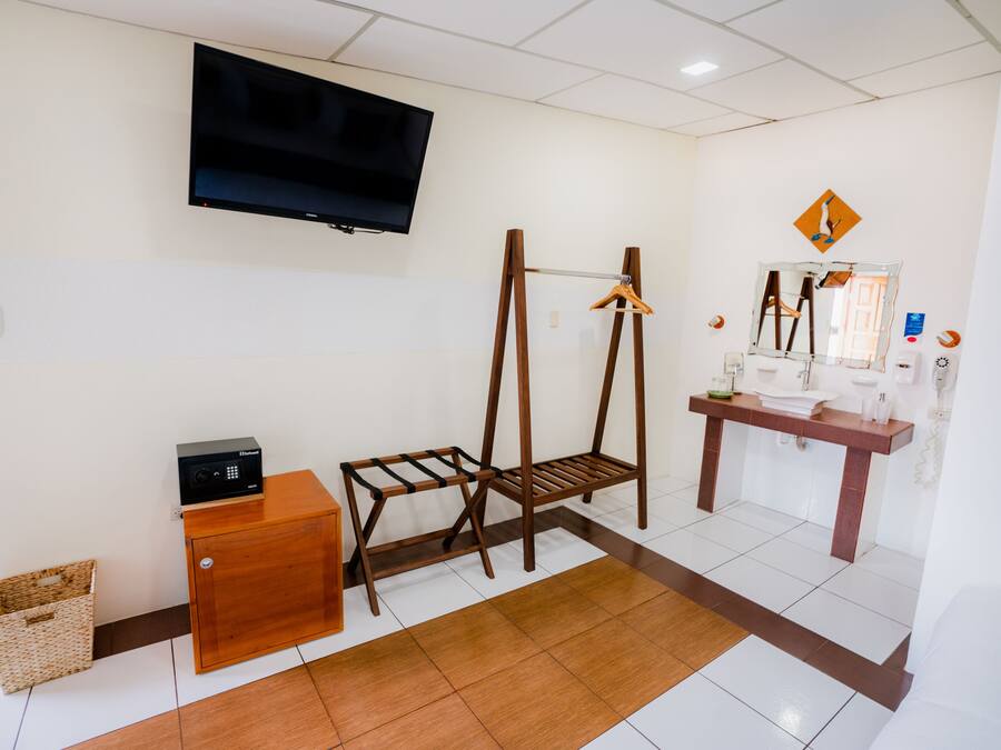 A room with a television mounted on the wall, a wooden desk with a computer, a wooden chair, a small wooden cabinet, and a hanging rack.