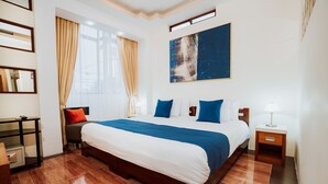 Ein Hotelzimmer mit einem großen Bett, einem Nachttisch, einem Schreibtisch mit Stuhl und einem fenster mit Vorhängen.