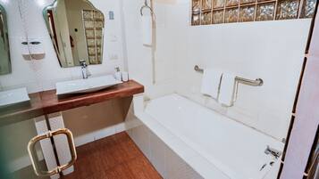 A bathroom with a white bathtub, a wooden vanity, a large mirror, and a glass shower enclosure.