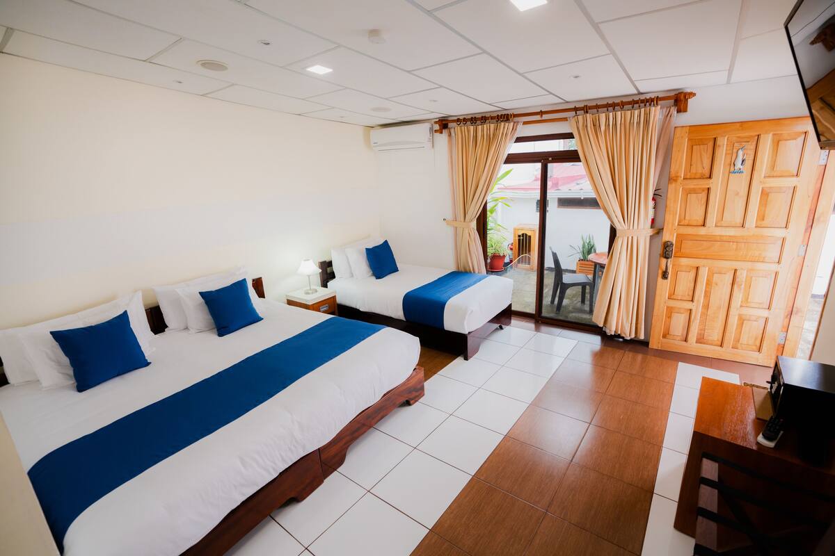 Een hotelkamer met twee bedden, een houten deur en uitzicht op buiten.