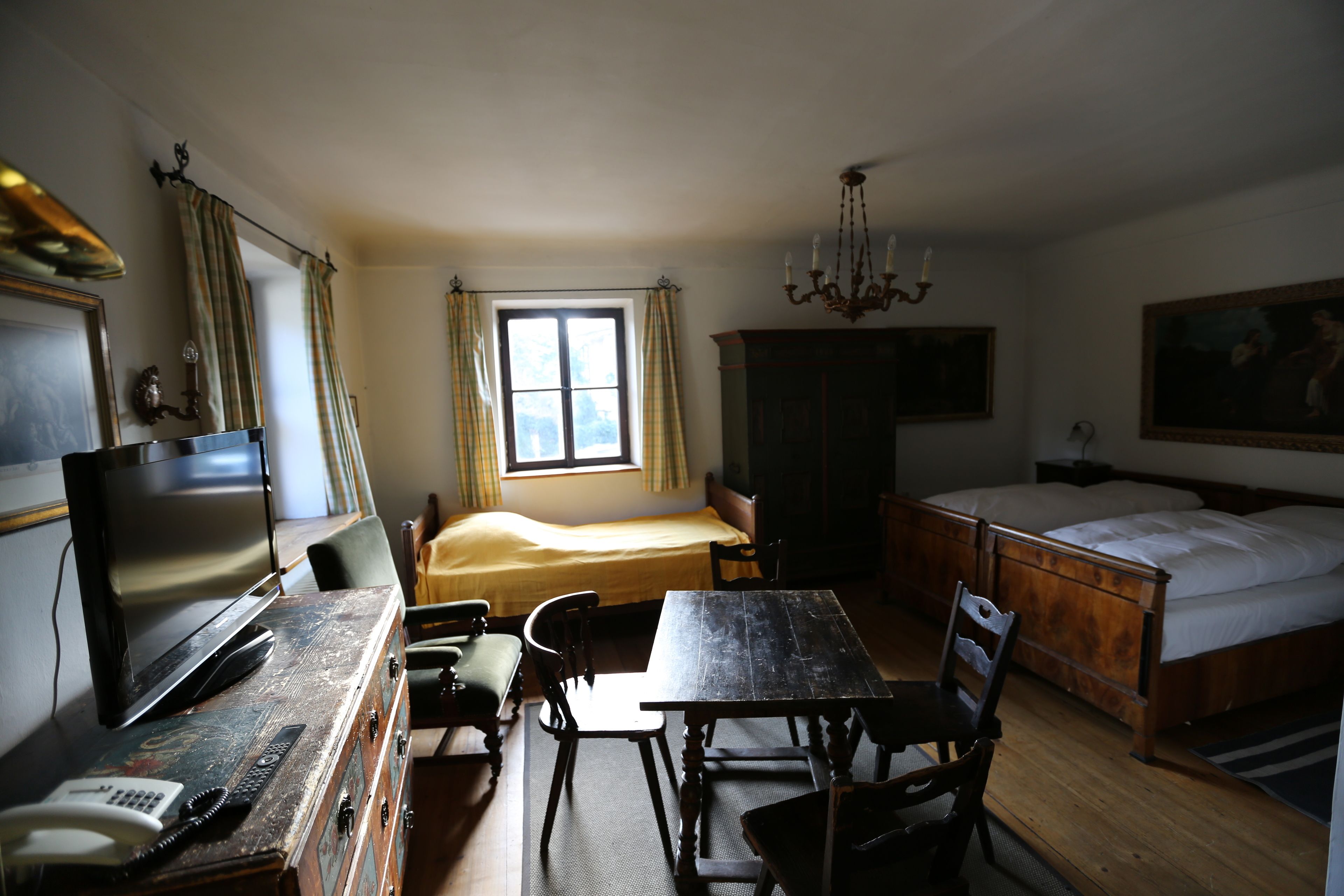 Une chambre comprenant un lit, un bureau avec un téléphone, une chaise, un téléviseur et une fenêtre avec des rideaux.