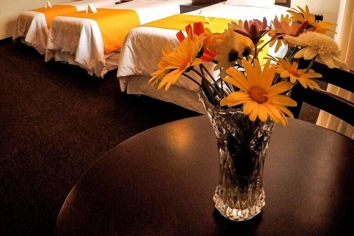 Ein Hotelzimmer mit zwei Betten, einem runden Tisch mit Blumen und einem dunklen Teppich.