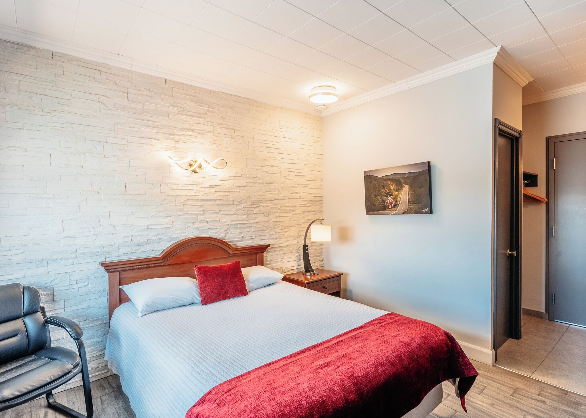 Una habitación de hotel con cama, mesita de noche, lámpara, silla y puerta.