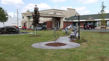 A building with a covered entrance, a parking lot, and a landscaped area with benches and a small tree.