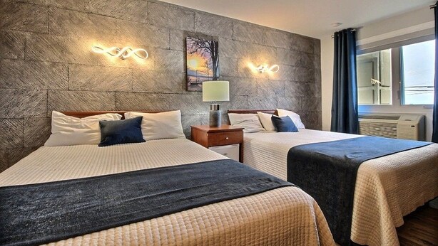 A hotel room with two beds, a stone-textured wall, a painting, and a window with curtains. - Hotel Motel Le Quiet (Lac-Megantic)