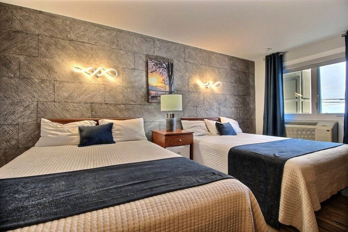 A hotel room with two beds, a stone-textured wall, a painting, and a window with curtains.