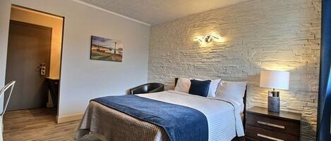 Un dormitorio con cama, mesita de noche, silla y puerta.
