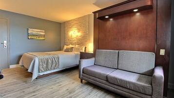 Un dormitorio con una cama, un sofá gris, una pared de madera y un cuadro.