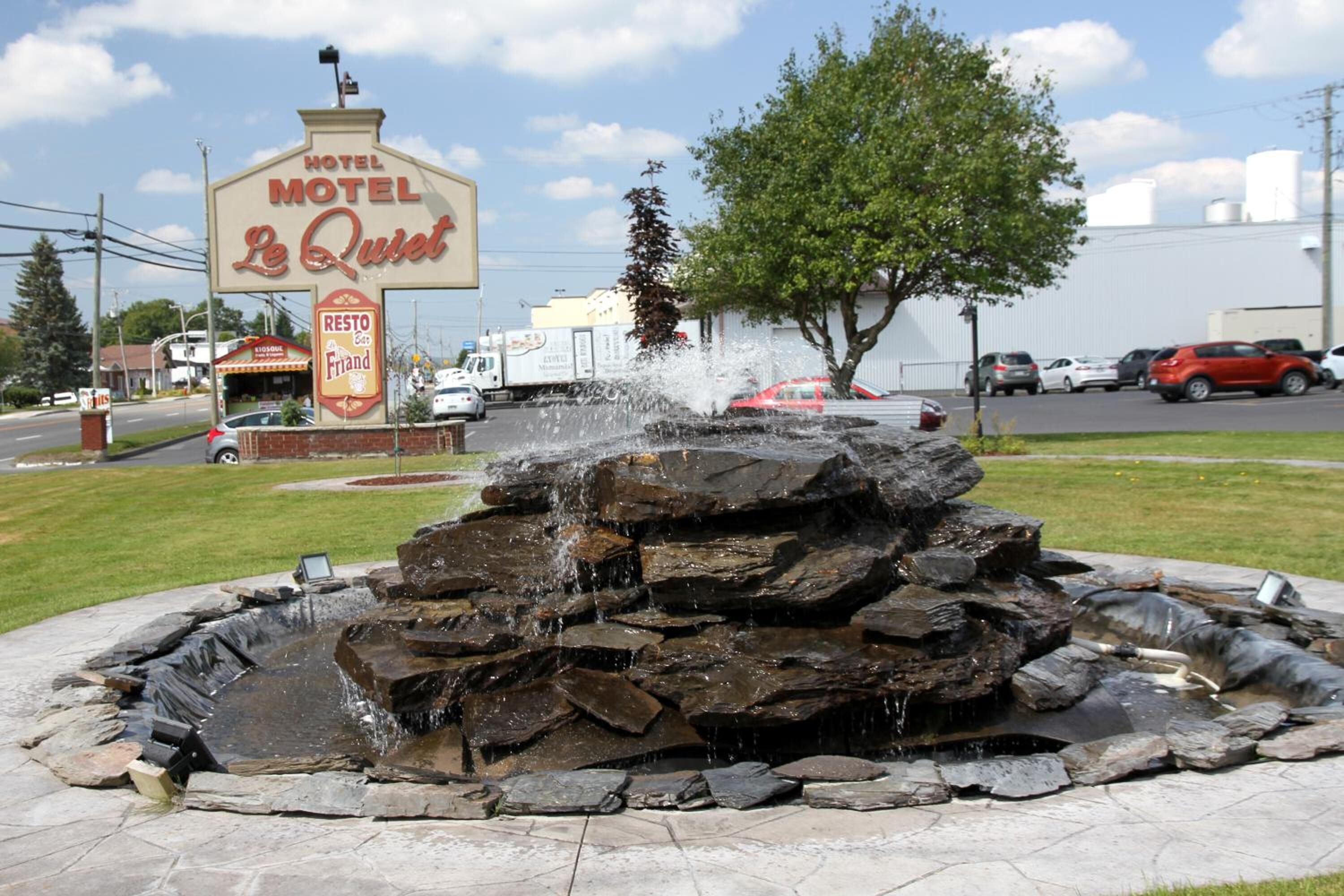 Cartel de motel que dice 'Le Quiet Motel', con un elemento decorativo de agua al frente.