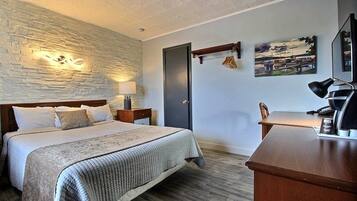 Une chambre d’hôtel avec un lit, un bureau, une lampe, un tableau et un mur en pierre.