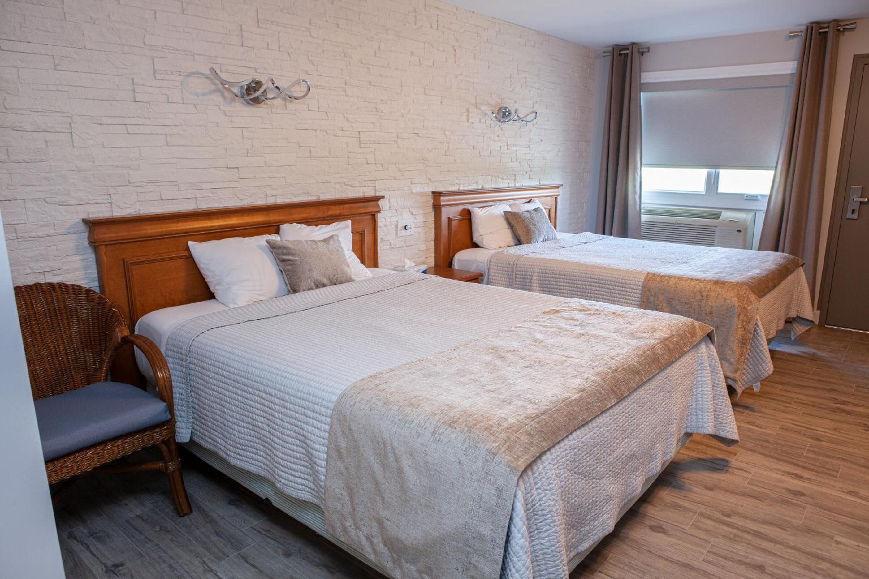 A hotel room with two beds, a brick wall, and a window with curtains.