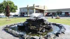 A landscaped fountain with a circular stone border, surrounded by a paved area. - Hotel Motel Le Quiet (Lac-Megantic)