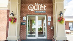 The exterior of Motel le Quiet with a reception area, brick facade, and flower baskets. - Hotel Motel Le Quiet (Lac-Megantic)