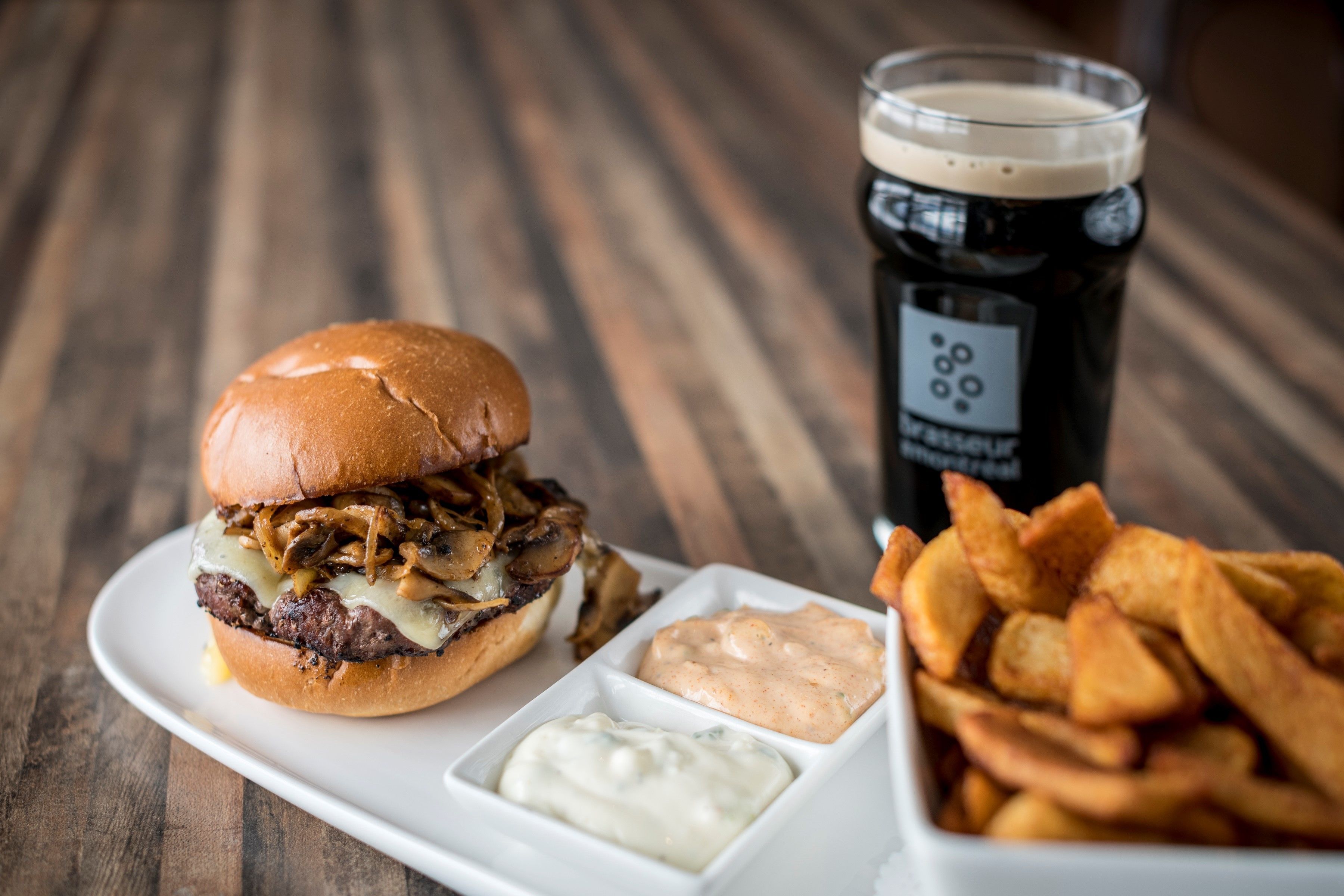 Un plato con una hamburguesa, papas fritas y una bebida sobre una mesa de madera.
