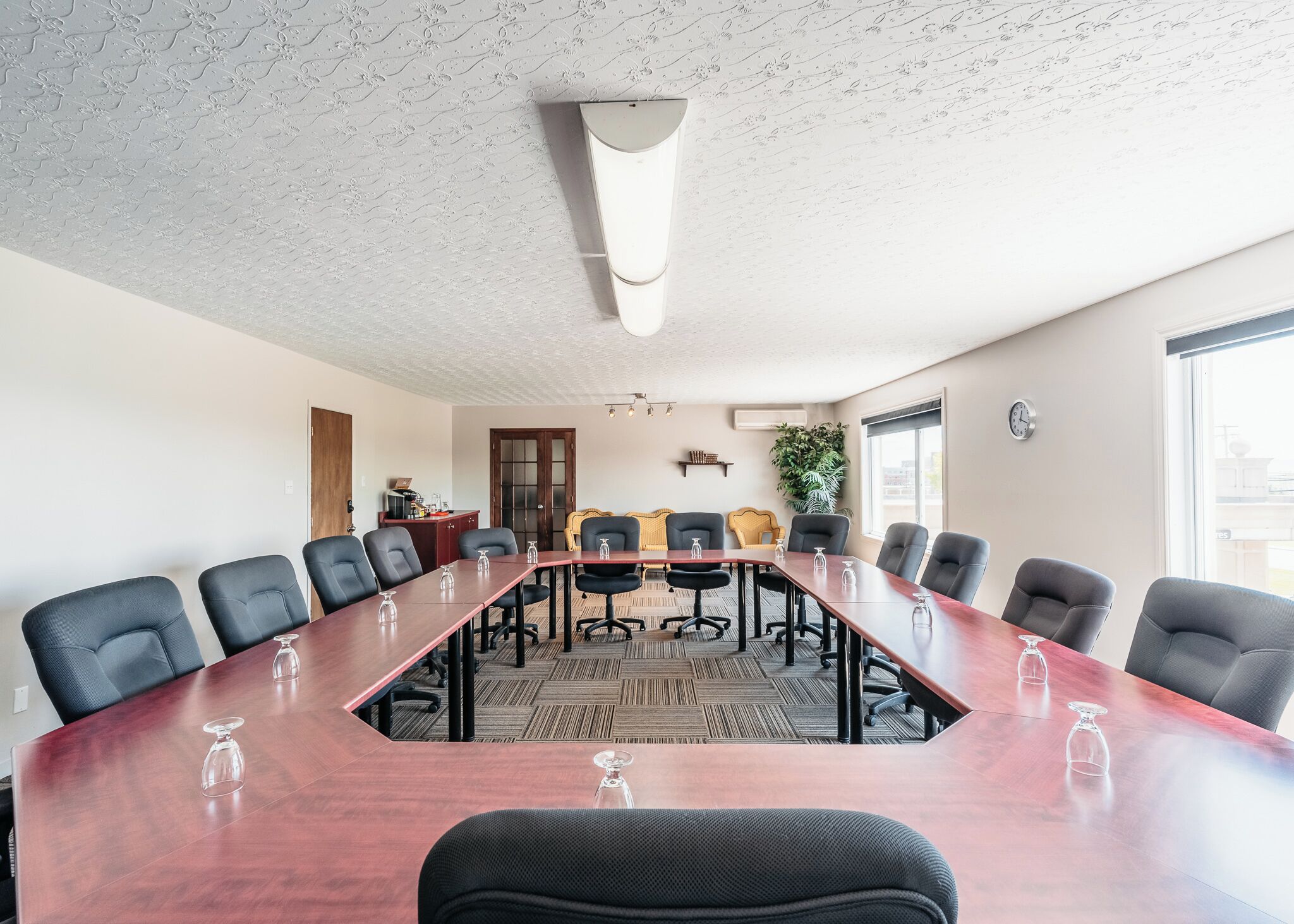 Un salón de conferencias con una larga mesa, sillas negras y una planta en maceta.