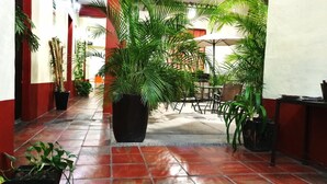 Un couloir doté d’un sol carrelé, de plantes en pot et d’un espace détente avec des chaises et des tables.