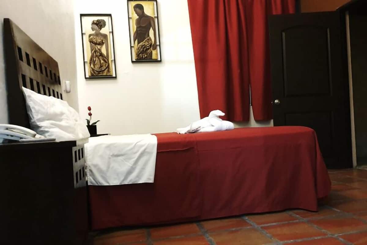 Een hotelkamer met een bed, een nachtkastje, een rood gordijn en twee ingelijste kunstwerken aan de muur.