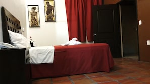 Une chambre d’hôtel avec un lit, une table de chevet, un rideau rouge et deux œuvres d’art encadrées accrochées au mur.