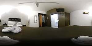 Une chambre d’hôtel avec un grand lit, une table de chevet, un téléviseur fixé au mur et une porte donnant sur une autre pièce.