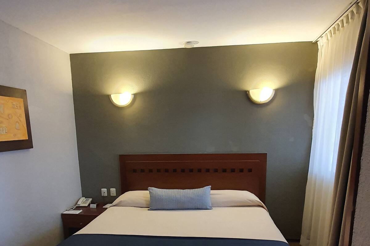 A hotel room with a bed, nightstands, a telephone, and wall-mounted lights.