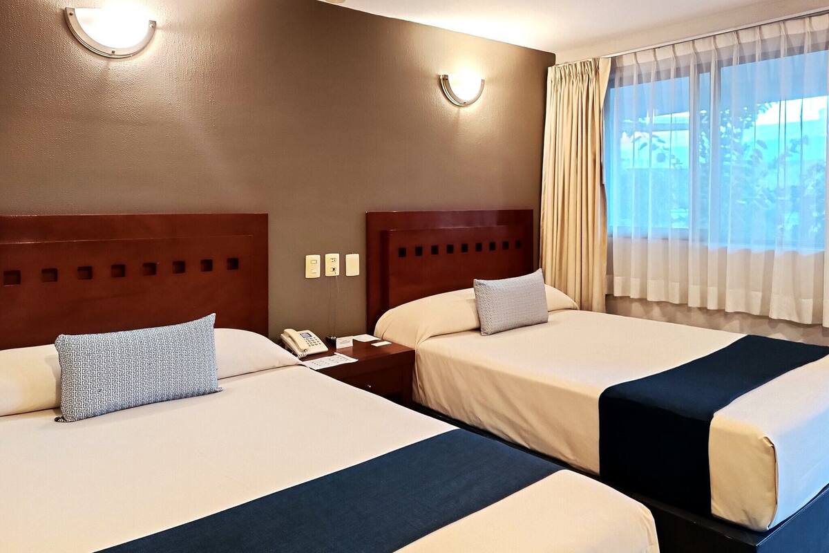 A hotel room with two beds, a nightstand with a phone, and a window with curtains.