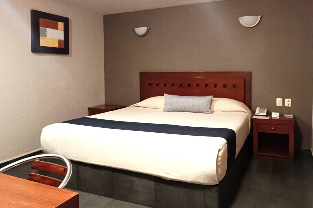 A hotel room with a bed, bedside tables, a desk, and a chair.