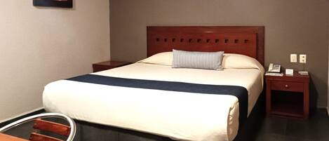 Quarto de hotel com cama, mesas de cabeceira, escrivaninha e uma cadeira.