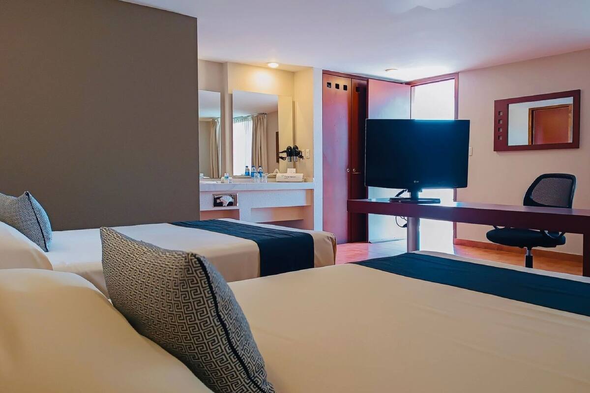 A hotel room with two beds, a desk with a TV, and a bathroom visible through an open door.