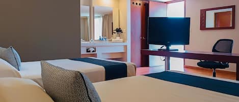 A hotel room with two beds, a desk with a TV, and a bathroom visible through an open door.