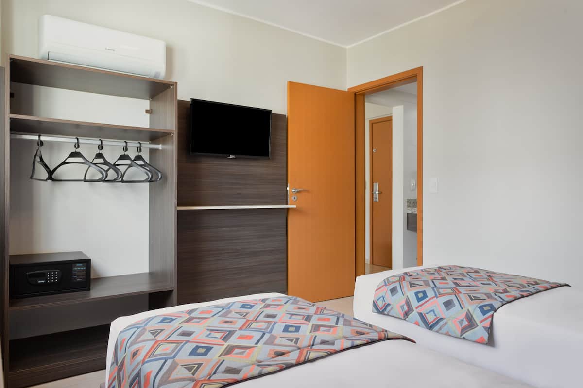 Ein Hotelzimmer mit Bett, Wandfernseher, Kleiderschrank und Tür.