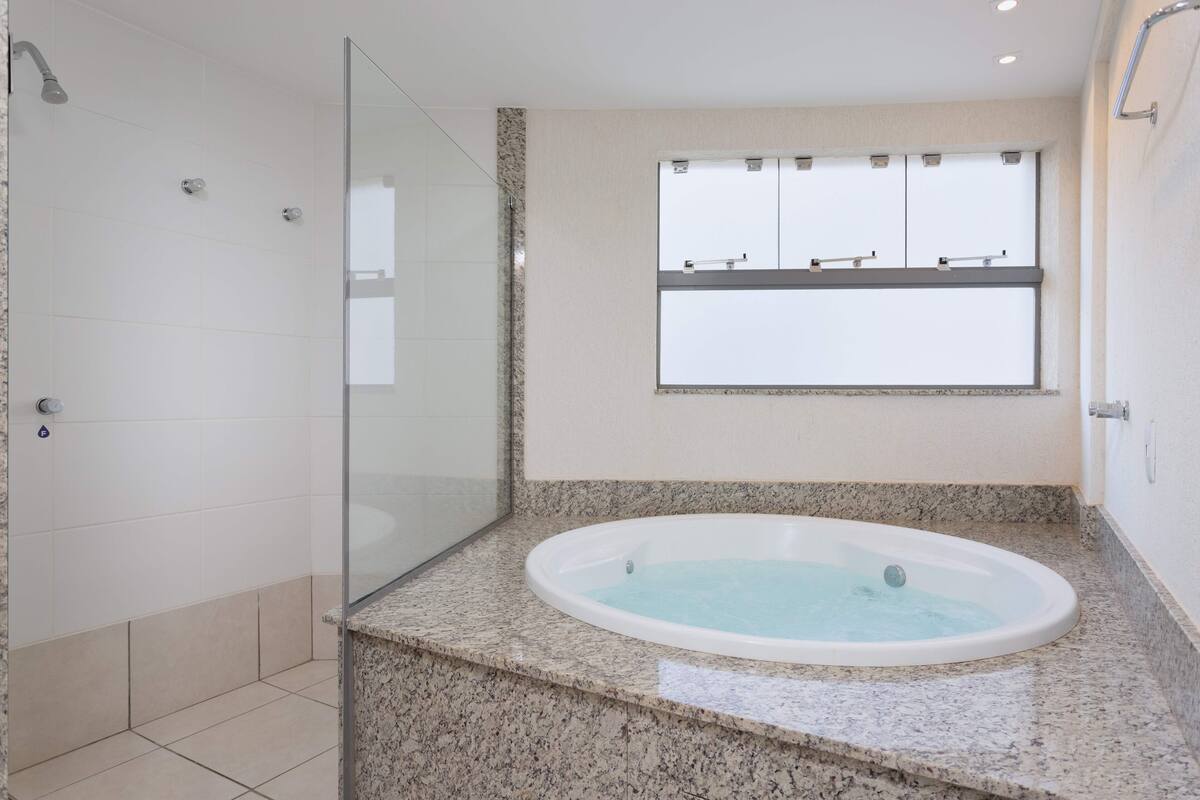 Ein modernes Badezimmer mit Duschkabine aus Glas, freistehender Badewanne und Fenster mit Blick zum Himmel.
