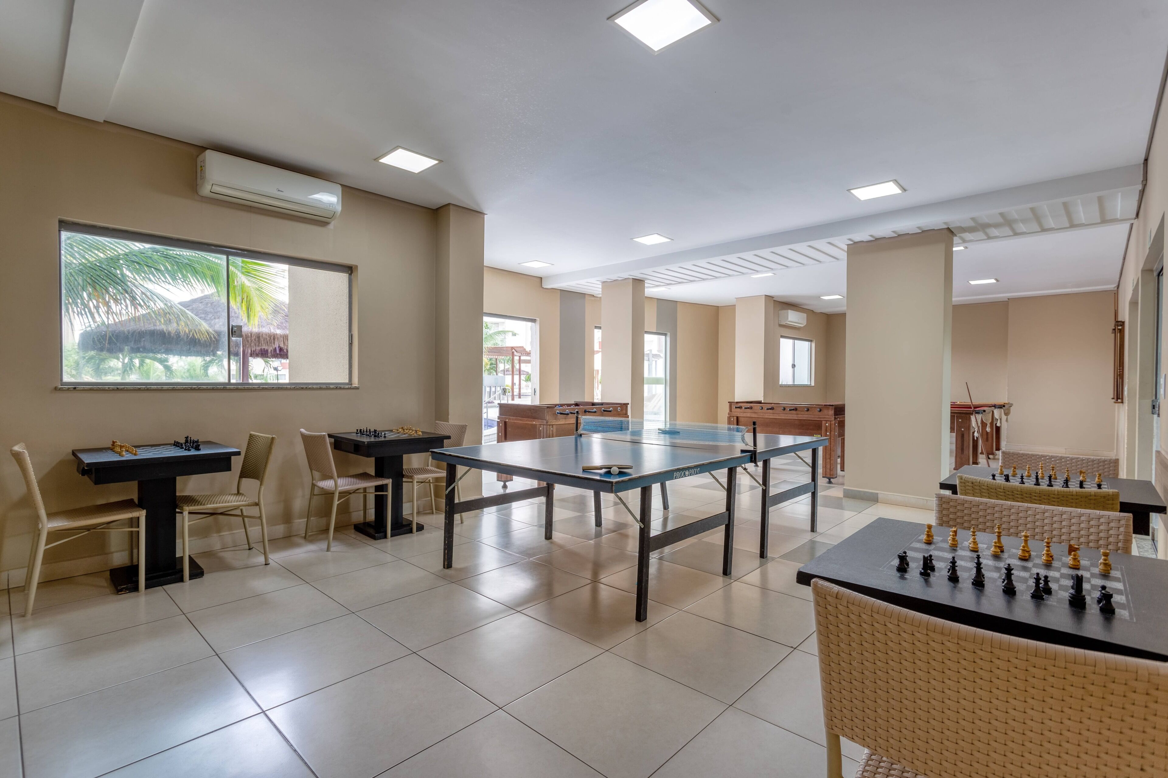 A spacious indoor area with multiple tables and chairs, air conditioning units, and large windows allowing natural light.