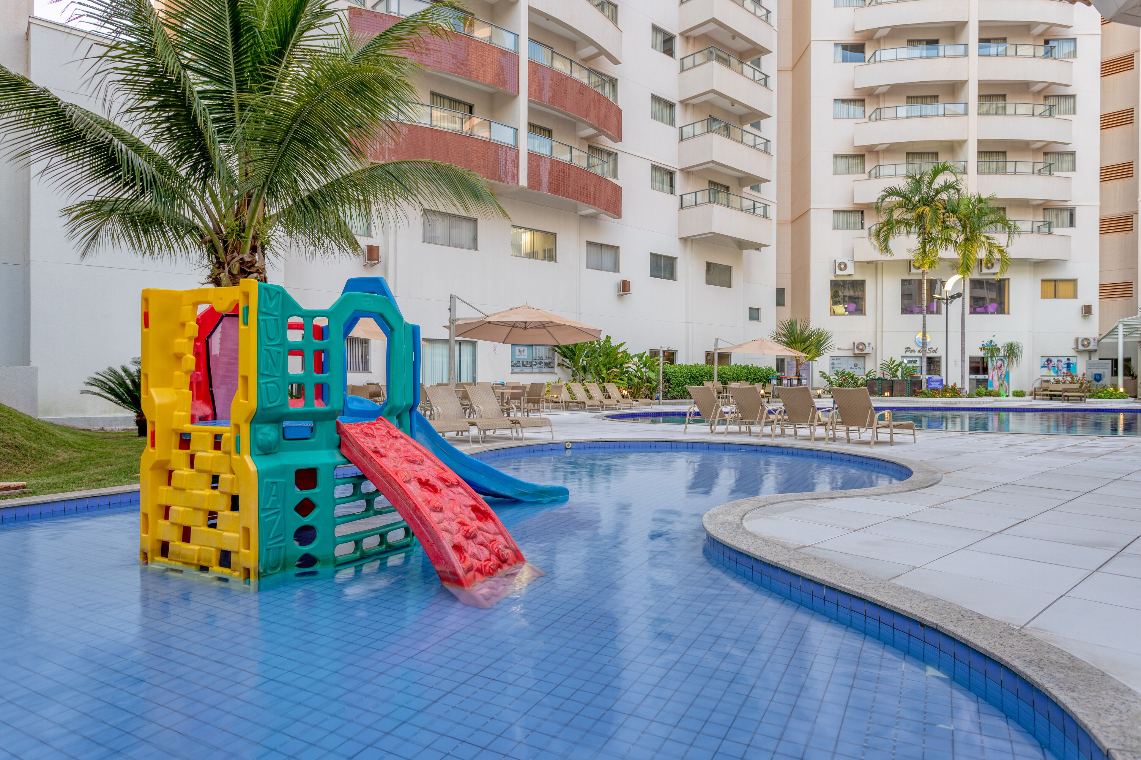 A pool area with a play structure, lounge chairs, and a palm tree.