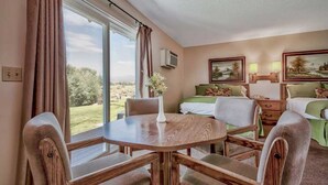 A hotel room with a dining table, two beds, a window with curtains, and a painting on the wall. - Walker River Lodge (Bridgeport)