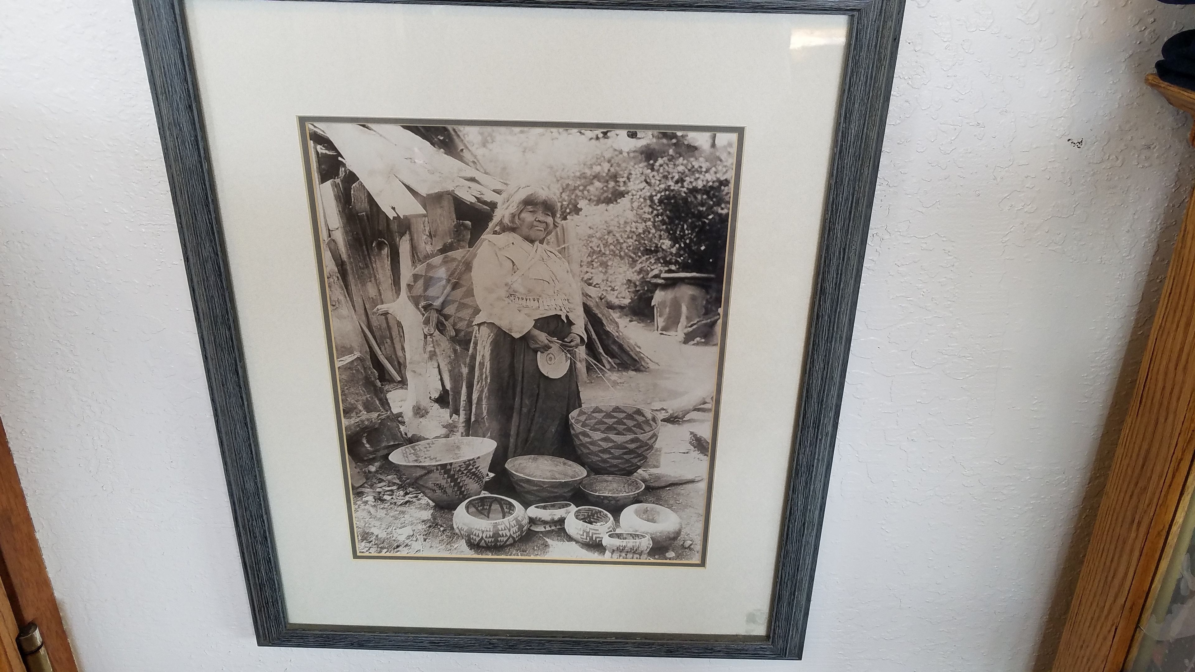 Fotografia a preto e branco emoldurada mostrando uma pessoa num espaço exterior, com várias tigelas e recipientes.