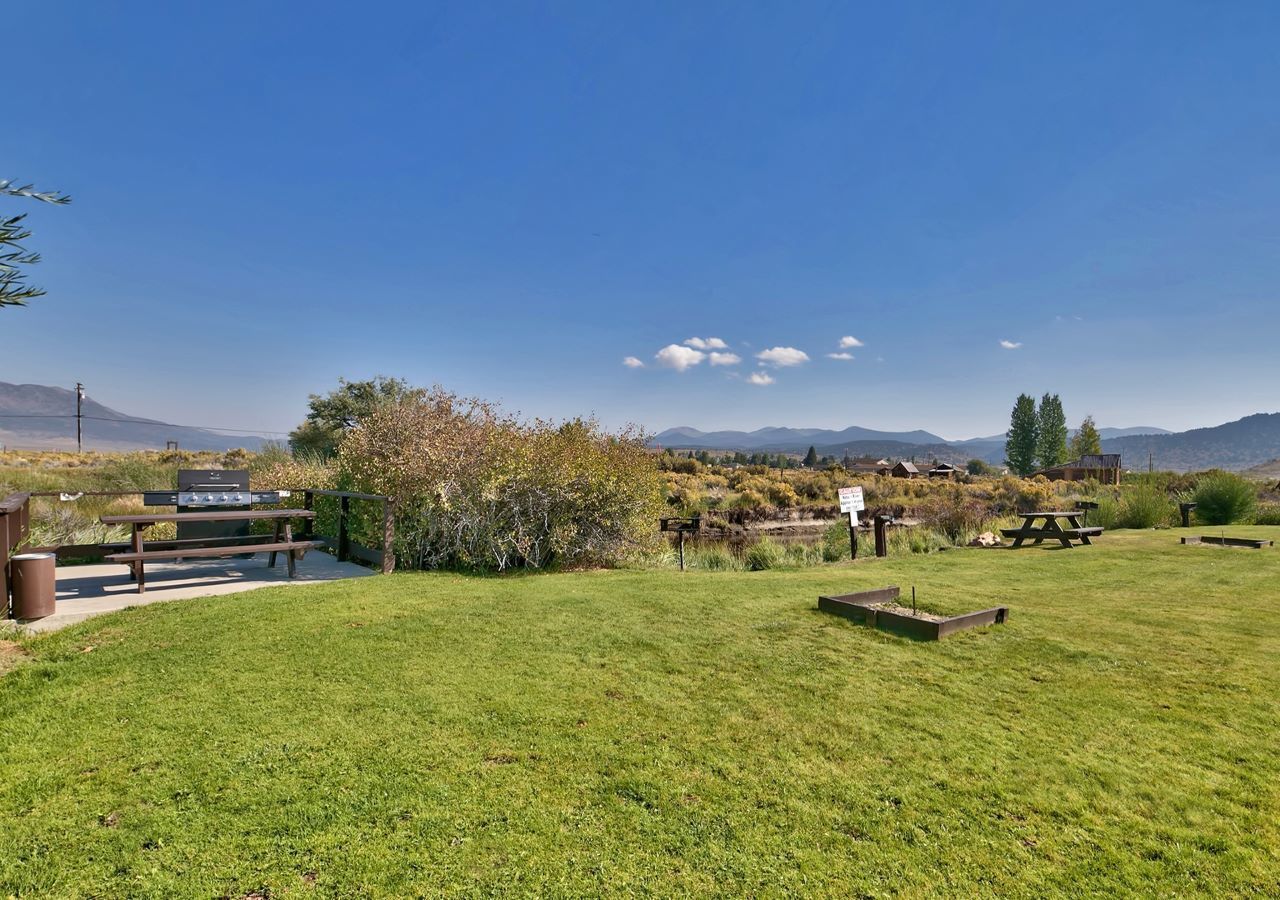 Un espacio al aire libre con césped, mesas de picnic y una parrilla.